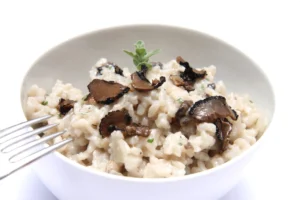 A bowl of truffle risotto garnished with fresh herbs and topped with slices of black truffle, presented on a white background.