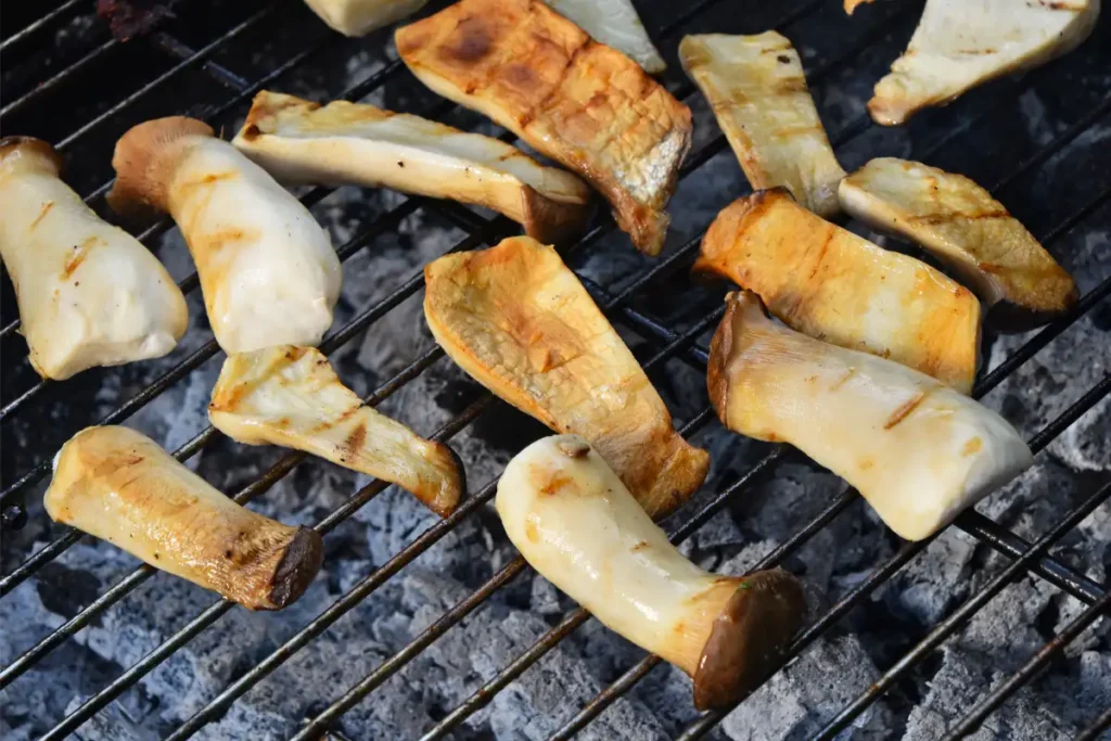 Oyster mushrooms grilling on a barbecue, showing char marks as they cook over the glowing coals.