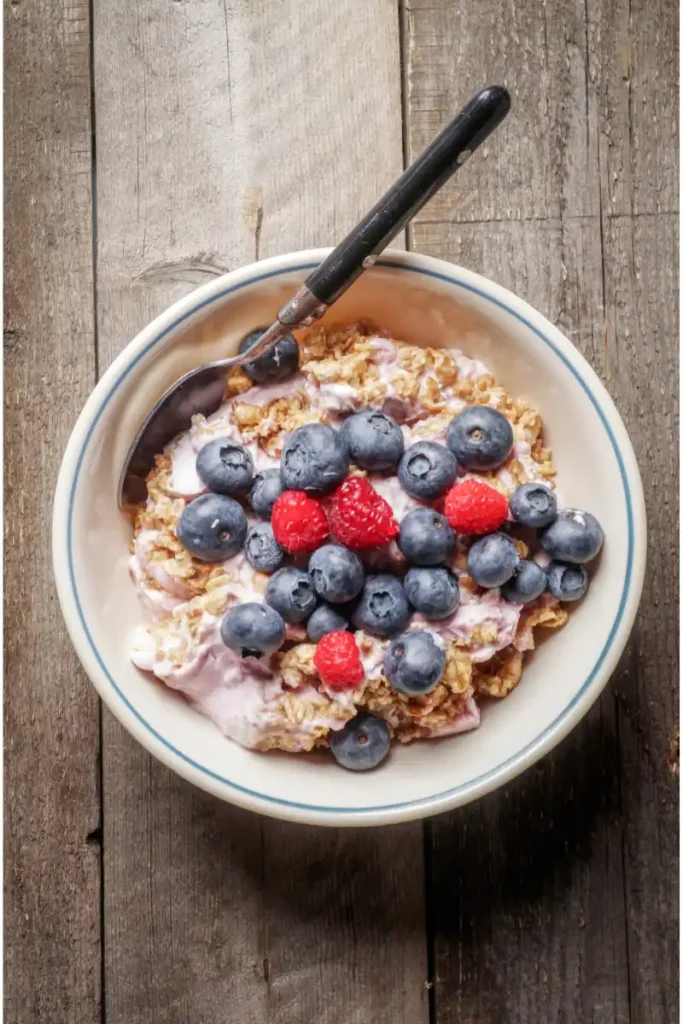 A bowl of oatmeal topped with fresh blueberries and raspberries on a rustic wooden surface, with a spoon resting inside the bowl.