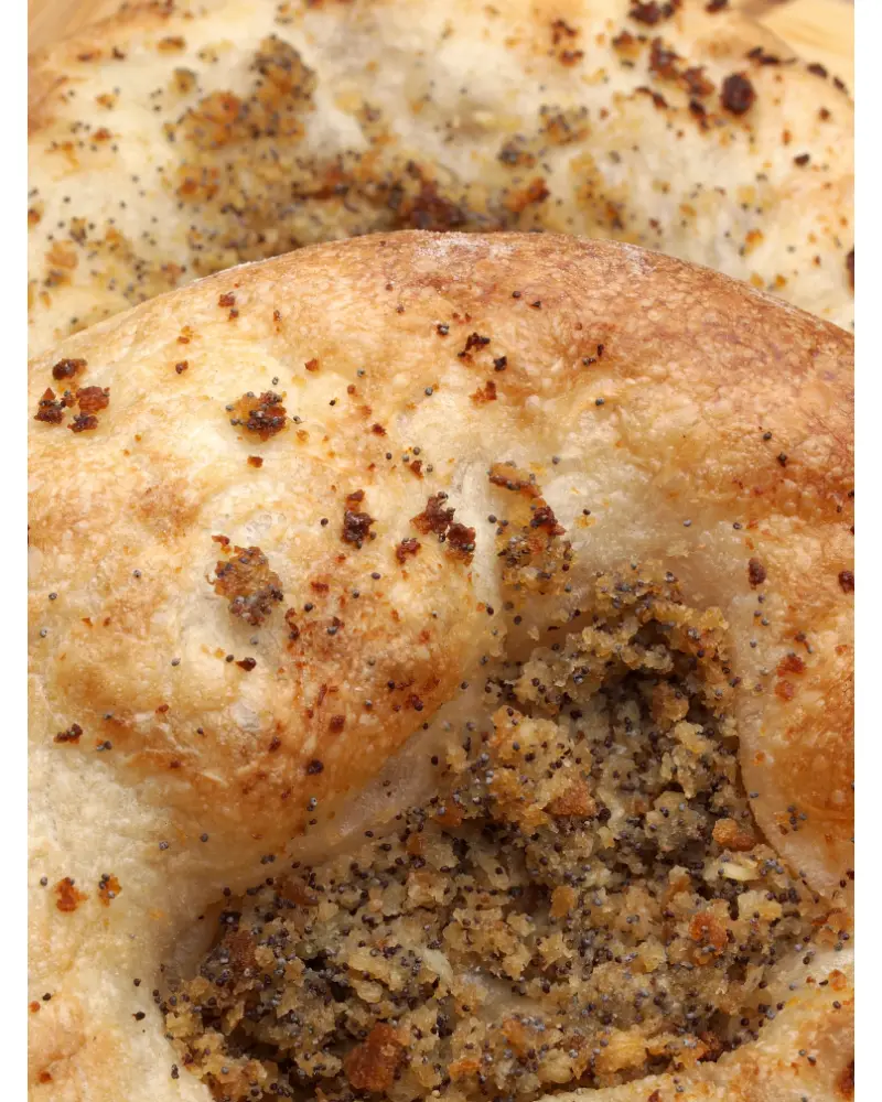 Extreme close-up of a golden-brown bialy bagel with a central pocket filled with poppy seeds and caramelized onions.