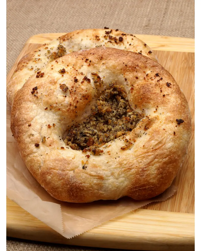 A bialy bagel with a toasted top and a center filled with poppy seeds and onions, resting on a wooden cutting board with parchment paper underneath.