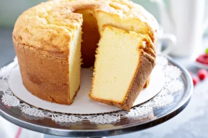 A freshly baked Bishop Cake, with one slice removed to reveal the moist, yellow interior, presented on a lace paper doily atop a metal serving tray