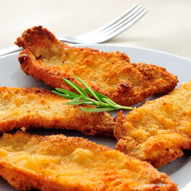 Crispy breaded milanesa steaks on a gray plate garnished with a sprig of rosemary, with a fork on the side.