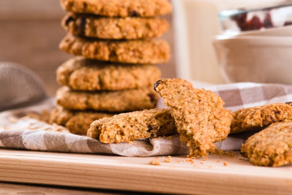 Stack of Cake Mix Cookies with one bitten, accompanied by a glass of milk and a bowl of dried fruits