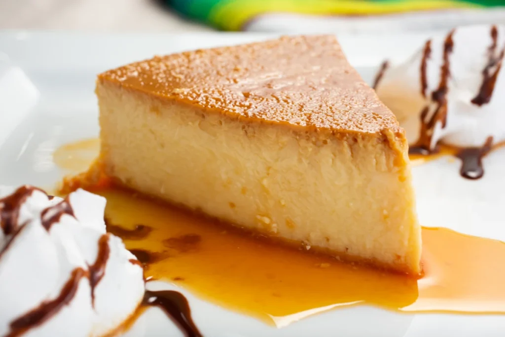 A close-up of a creamy coconut flan slice on a white plate, drizzled with caramel and chocolate sauce, garnished with whipped cream.