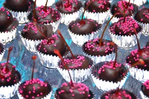 A tray of chocolate-covered cherries with pink sprinkles, each in a silver foil cup.