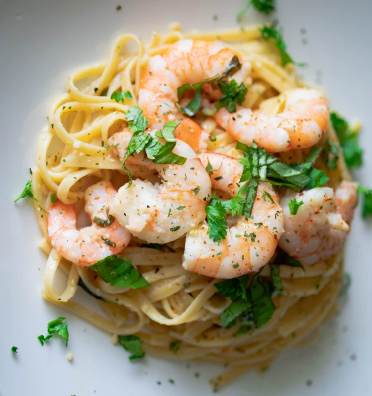 A plate of shrimp pasta, topped with fresh parsley, highlighting the contrast between the pink shrimp and the creamy, light-colored pasta.