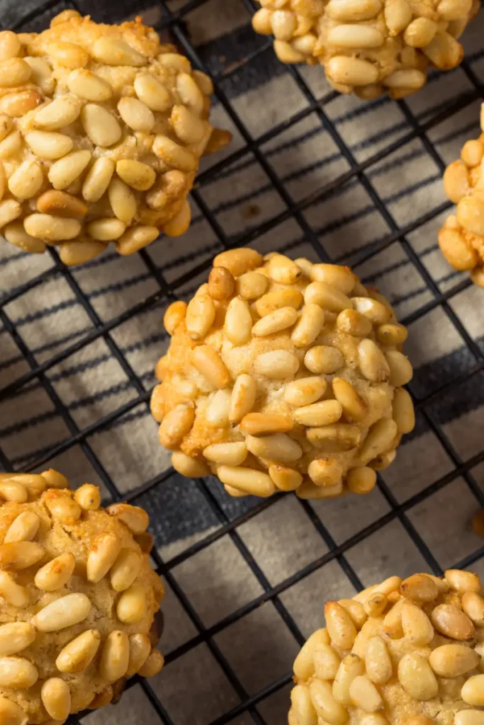 Close-up view of pignoli cookies with a generous coating of pine nuts, displayed on a cooling rack.