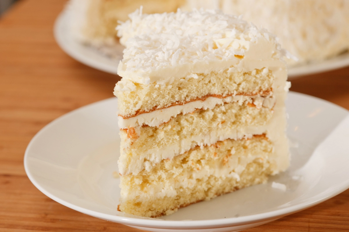 Slice of coconut cake on a white plate.