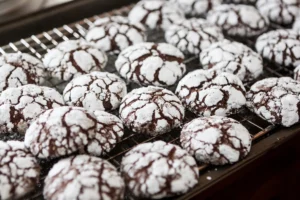 A batch of Cool Whip cookies with cracked powdered sugar tops cooling on a wire rack.