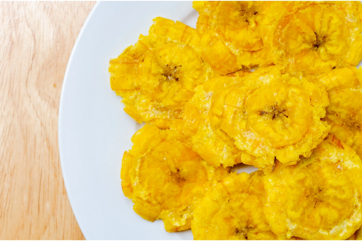 A plate of patacones, or twice-fried green plantains, with a crispy golden-brown texture, served on a white plate with a wooden table background.