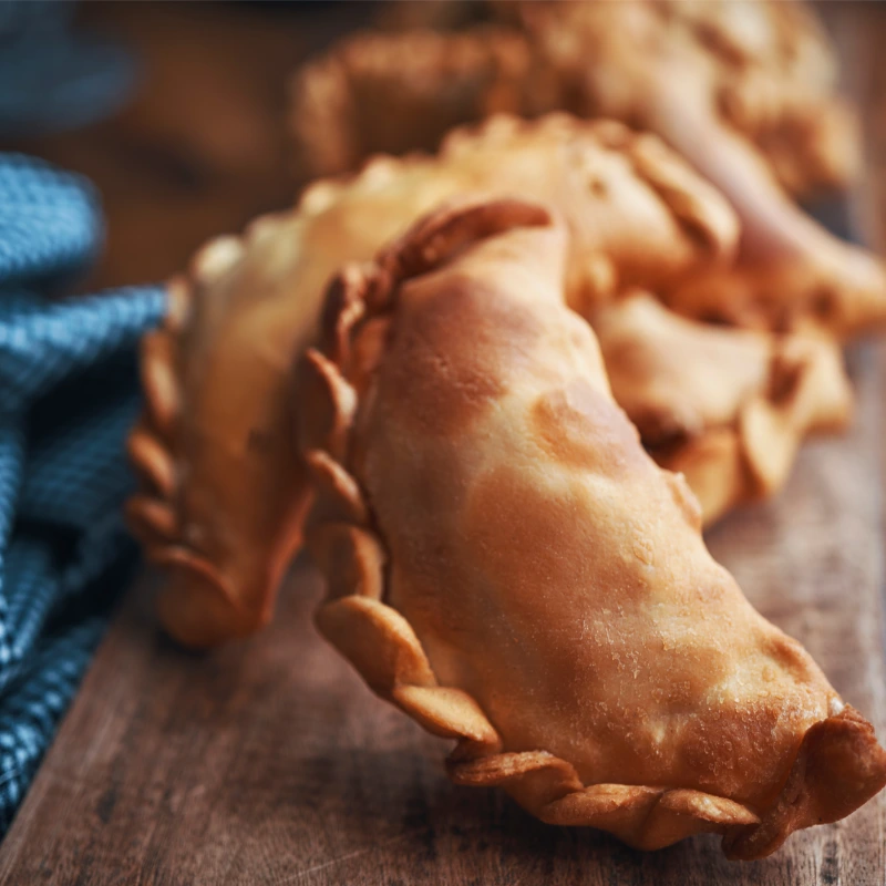 Close-up of a row of deep-fried pumpkin empanadas with a golden crust, on a wooden surface.