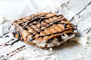 A fluffernutter sandwich, split open to show creamy white filling and drizzled with dark chocolate syrup, on a parchment-lined surface with chocolate streaks.