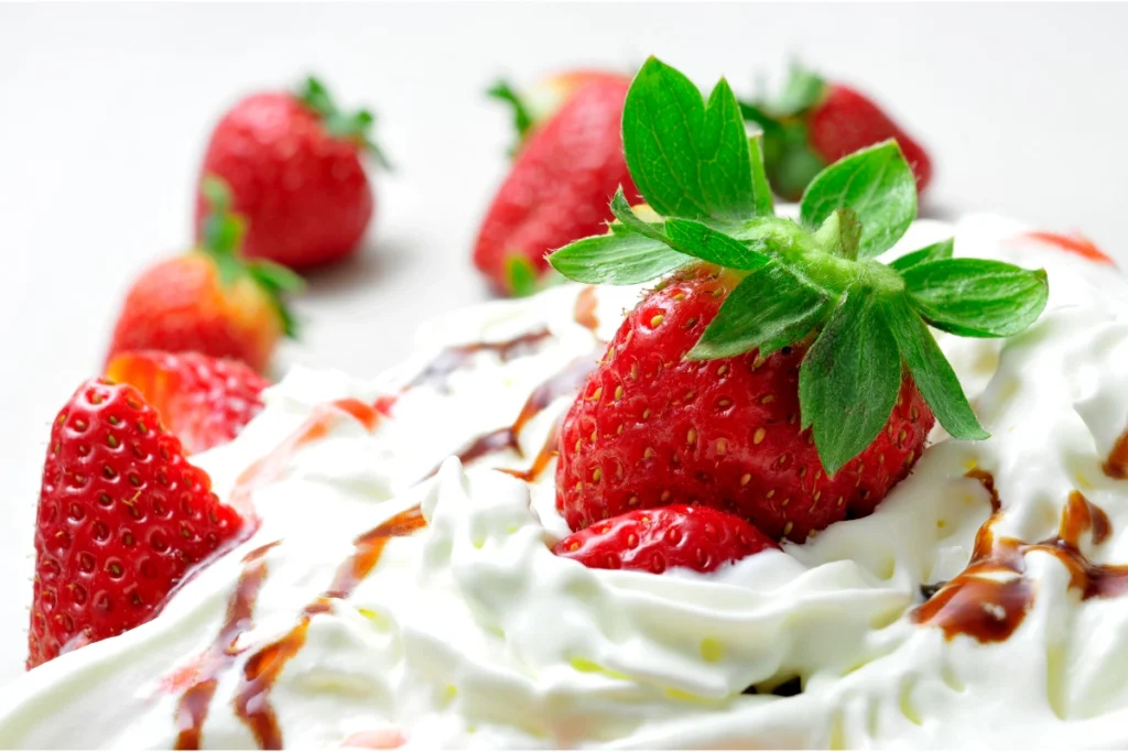 Fresh strawberries with green leaves on top of whipped cream, drizzled with chocolate syrup.