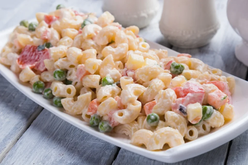 Hawaiian Macaroni Salad served on a white dish, featuring macaroni with peas, carrots, and a creamy sauce on a wooden table background.