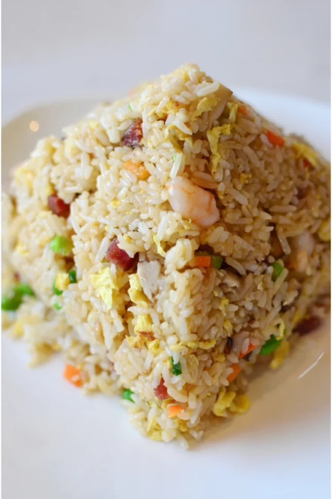 Heaping portion of Yangzhou Fried Rice with shrimp, egg, ham, and diced vegetables on a white plate.