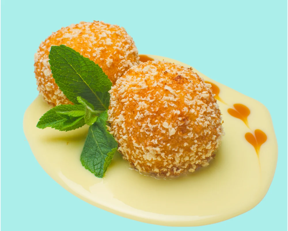 Two scoops of deep-fried ice cream on a yellow sauce with a mint leaf garnish, accented by heart-shaped sauce designs on a teal background.