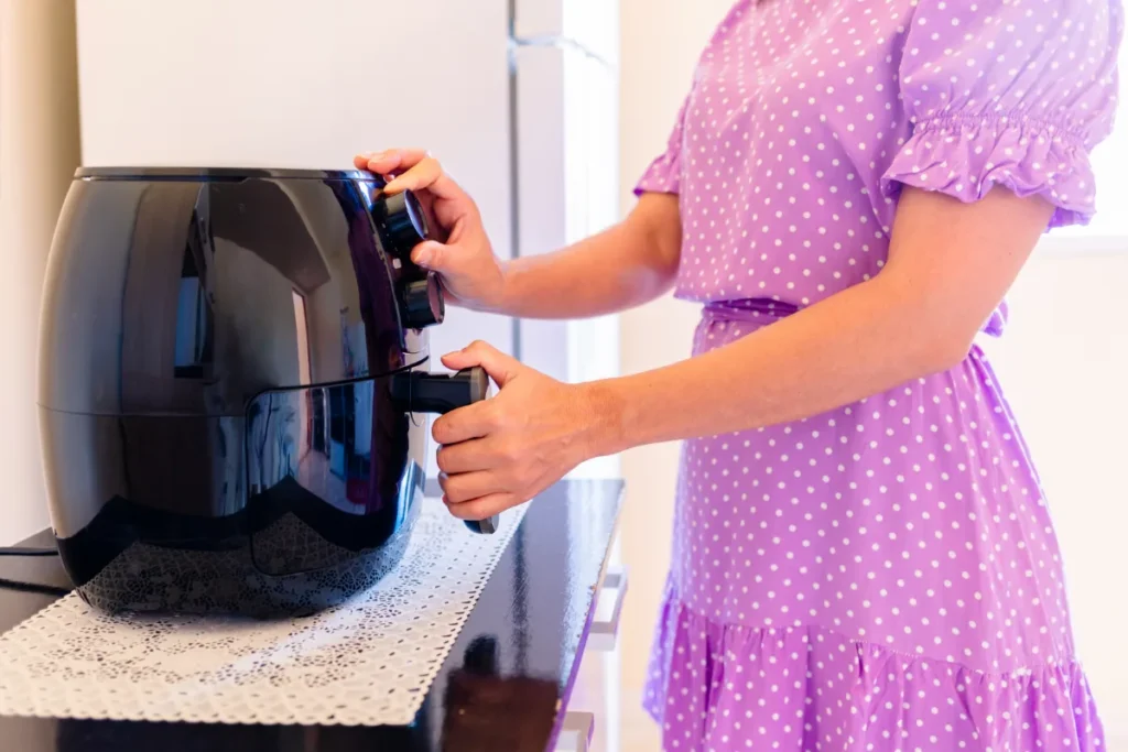 Person in a purple polka-dot dress using an air fryer in a kitchen setting