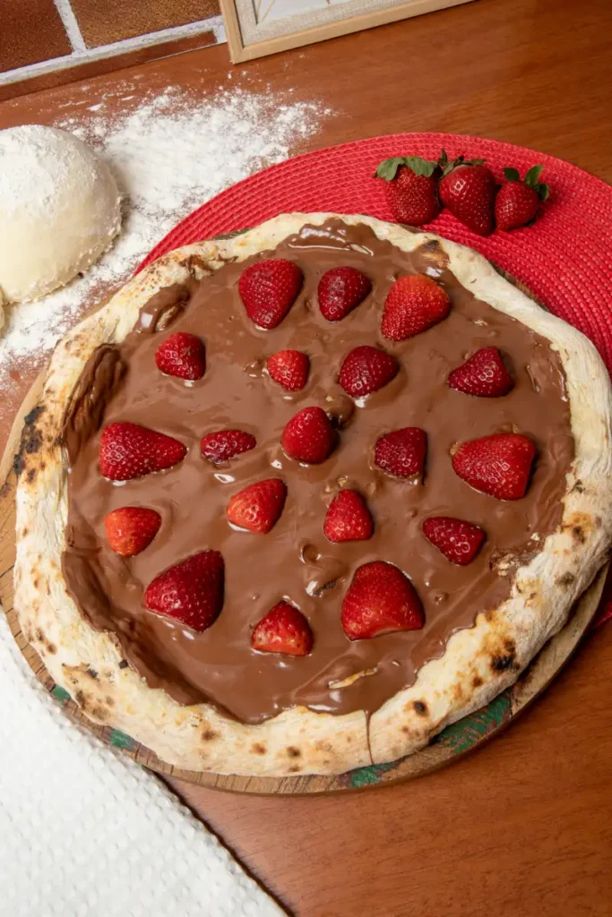 A freshly prepared chocolate pizza topped with whole strawberries is placed on a wooden paddle