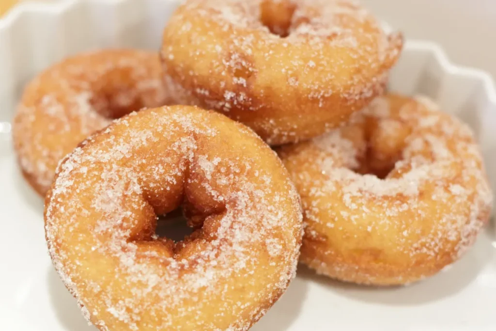 A trio of sugar-dusted doughnuts with a deep golden color, resting on a white scalloped plate, highlighted by their soft texture and round shapes.