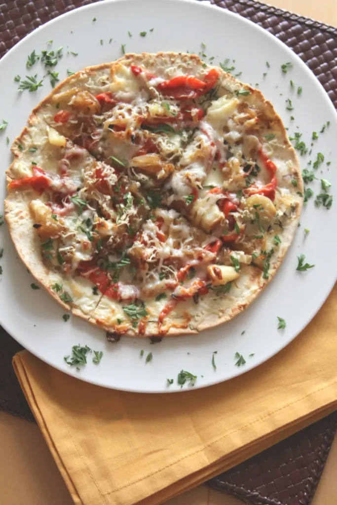 A thin crust pizza with assorted toppings, including bell peppers and onions, on a white plate over a yellow napkin and dark woven placemat.