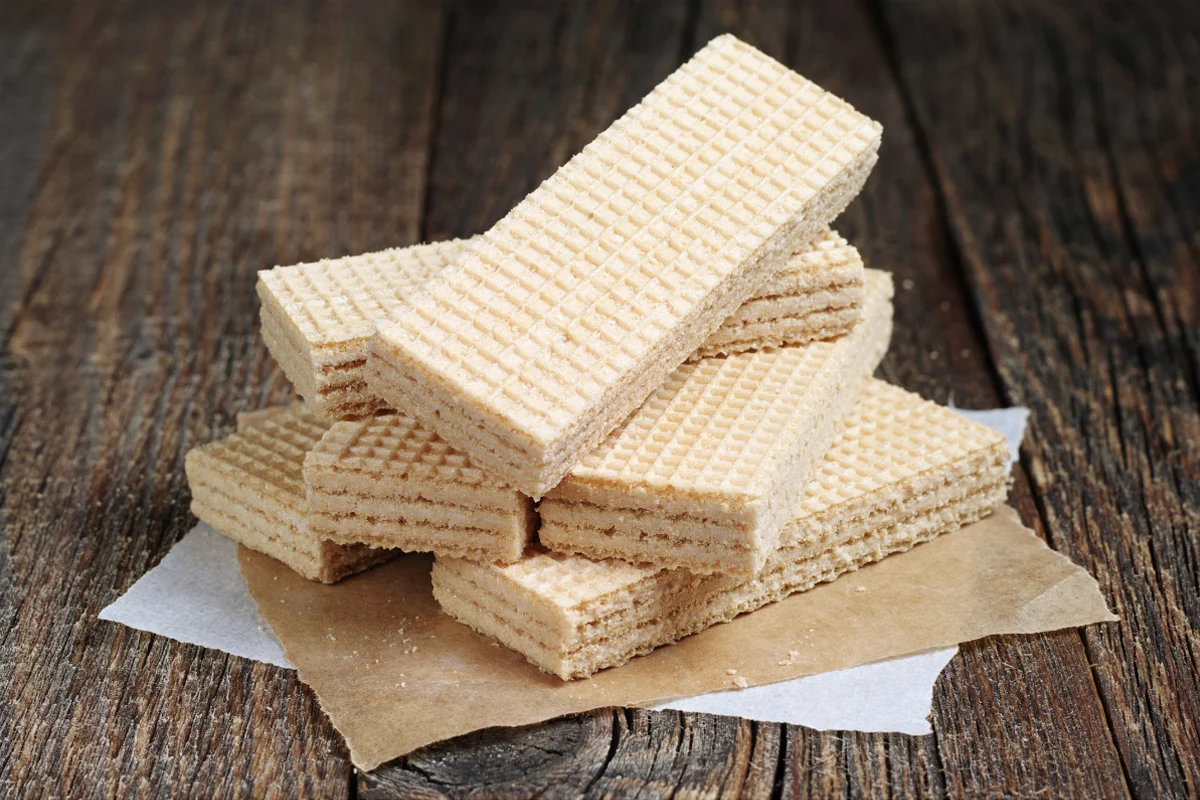 A stack of light-colored wafer cookies placed on a piece of parchment paper, with a rustic wooden table surface as the background.