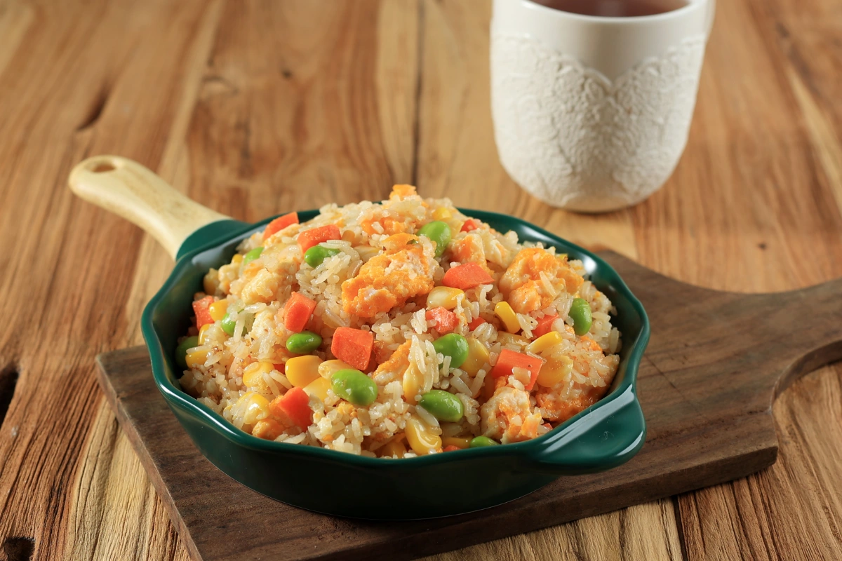 Yangzhou Fried Rice served in a green dish on a wooden cutting board, with a white mug in the background.