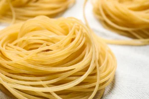 Close-up view of uncooked Capellini pasta nests arranged on a textured white cloth.