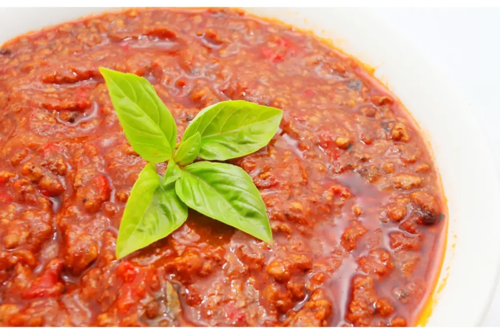 A close-up of tomato gravy topped with a fresh basil leaf, served in a white dish.