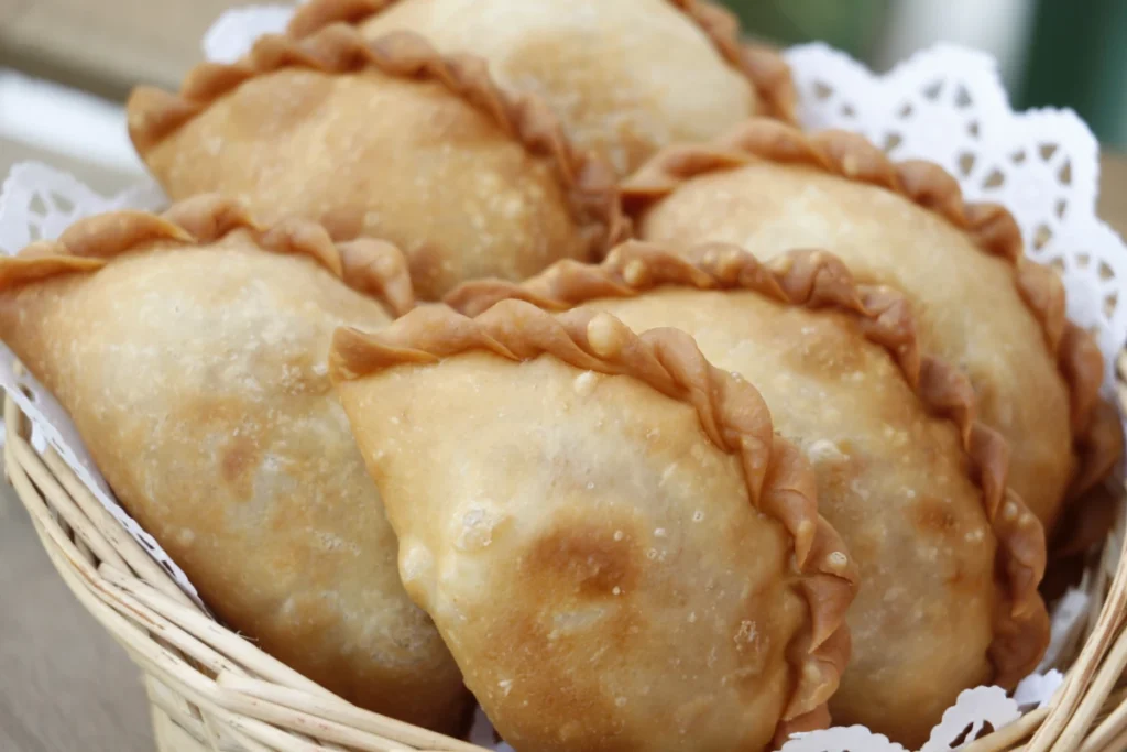 A basket of golden-brown empanadas lined with lace paper.