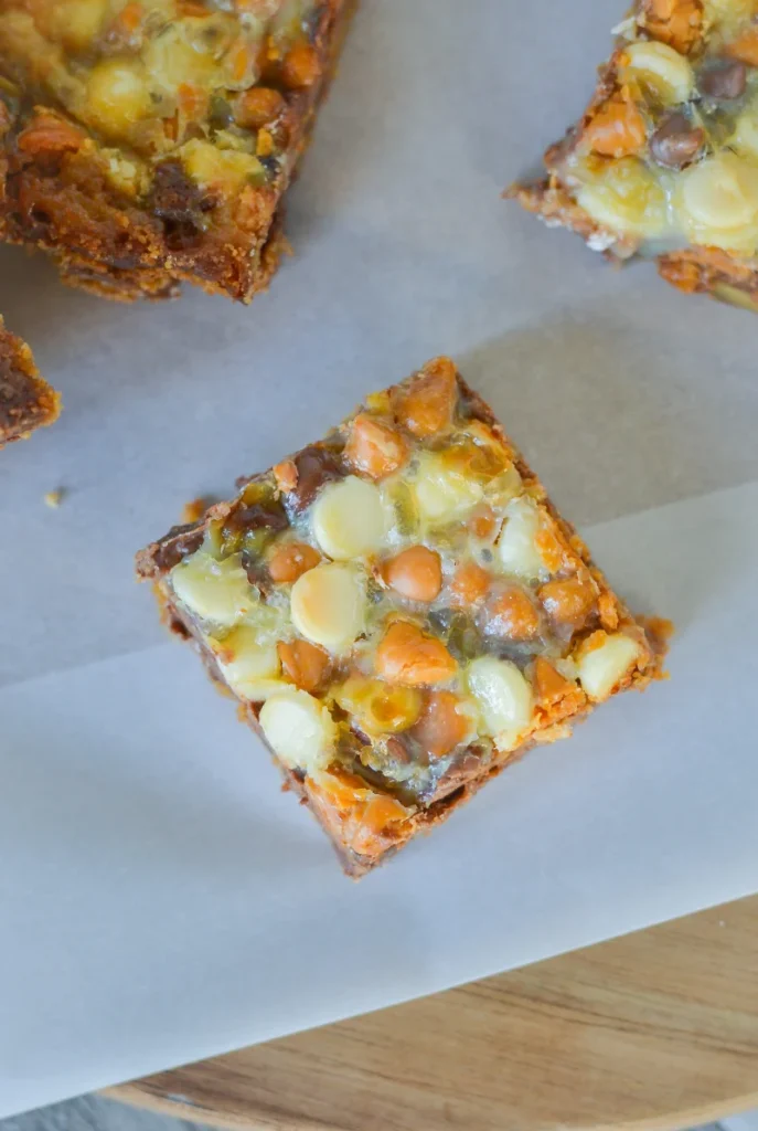 Close-up view of a single 7 layer bar showcasing a gooey layer with a variety of nuts and chocolate chips, placed on parchment paper.