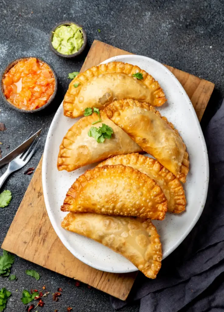 A plate of empanadas with guacamole and salsa on the side.