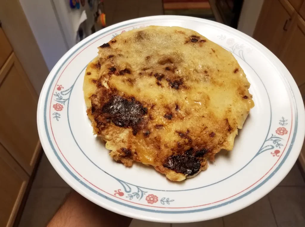 A single pupusa on a white plate with a floral design.