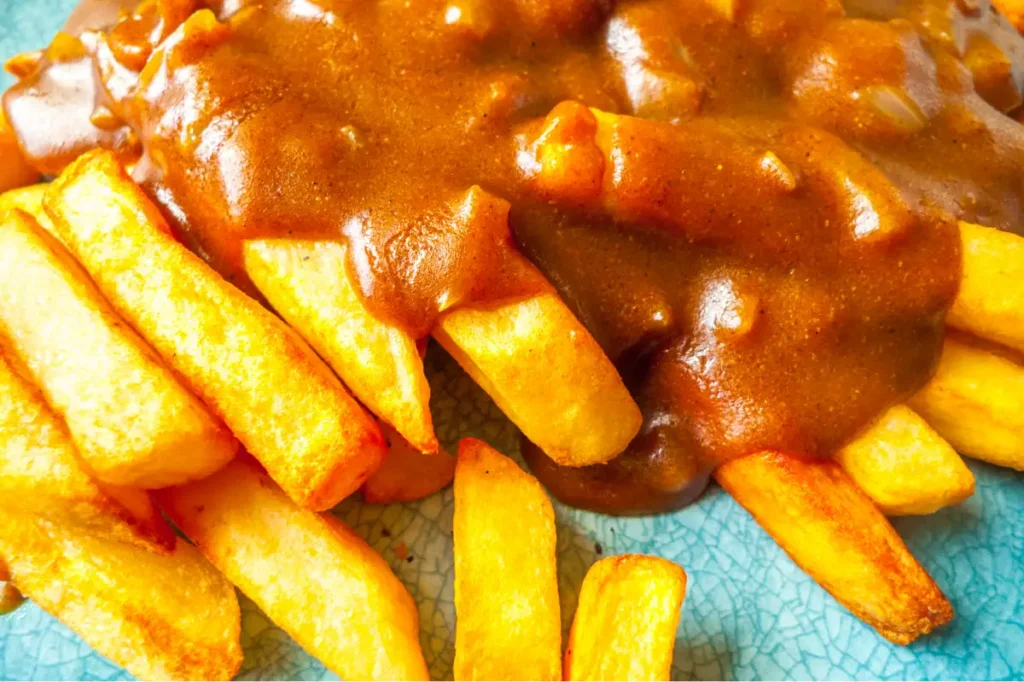 Close-up of thick-cut fries covered in katsu sauce on a blue plate.