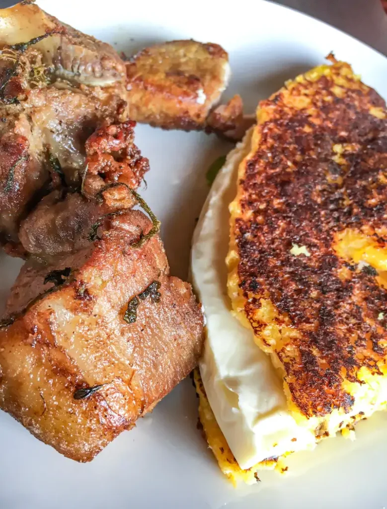 A plate featuring a grilled cachapa filled with melted cheese next to crispy fried meat chunks.