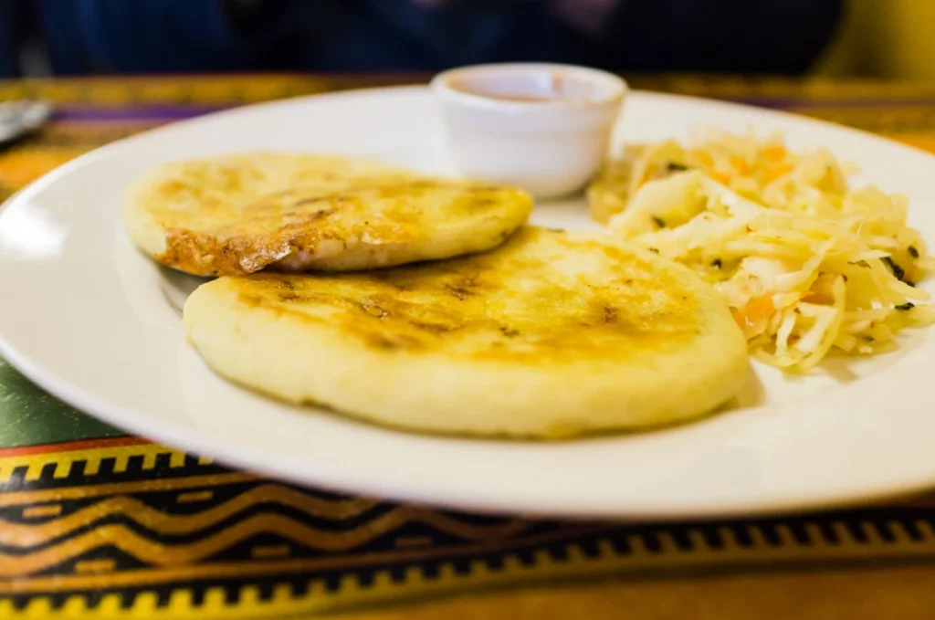 Two pupusas with curtido and salsa on a white plate.