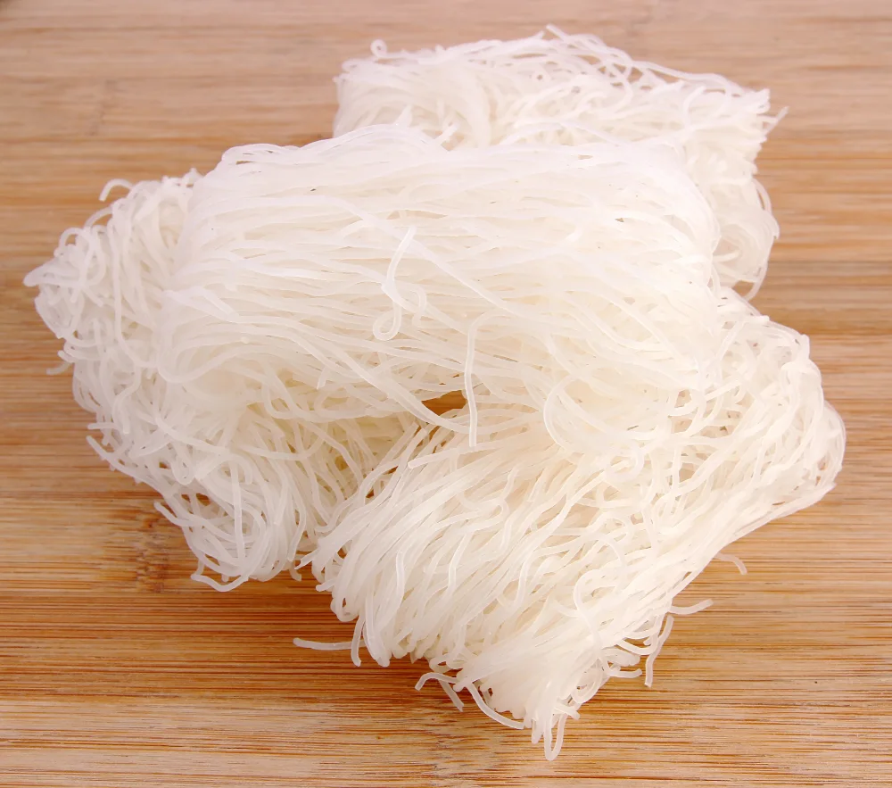 Piles of uncooked white vermicelli noodles on a wooden surface.