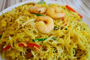 A plate of shrimp vermicelli with yellow noodles, vegetables, and sesame seeds.