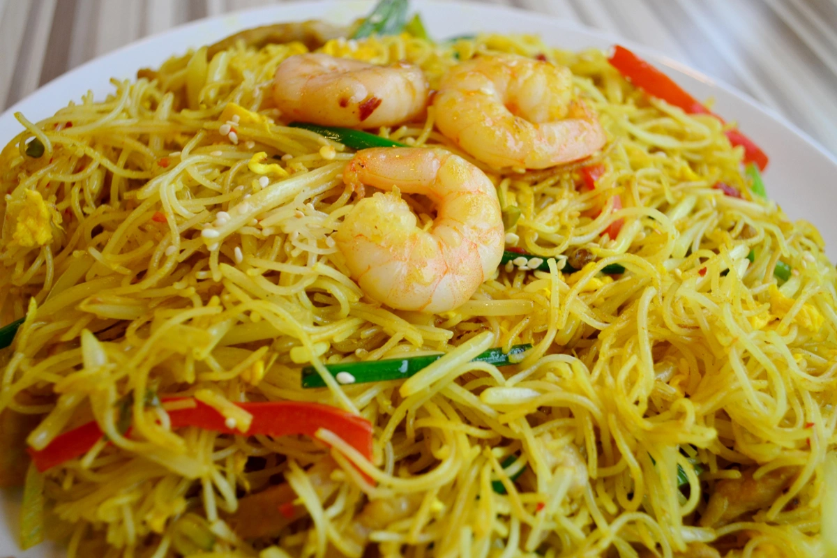 A plate of shrimp vermicelli with yellow noodles, vegetables, and sesame seeds.