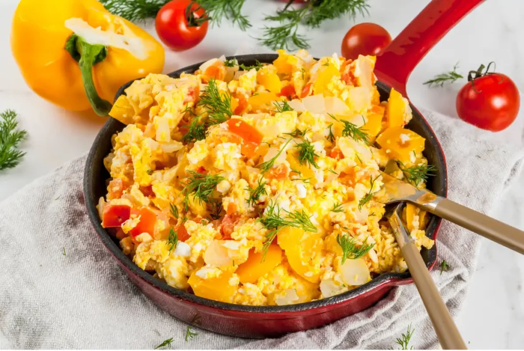 Scrambled eggs with bell peppers and tomatoes in a skillet.