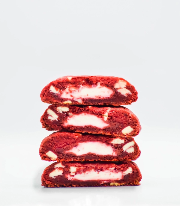 Four red velvet cookies with cream cheese filling and white chocolate chips, stacked on top of each other against a plain white background.