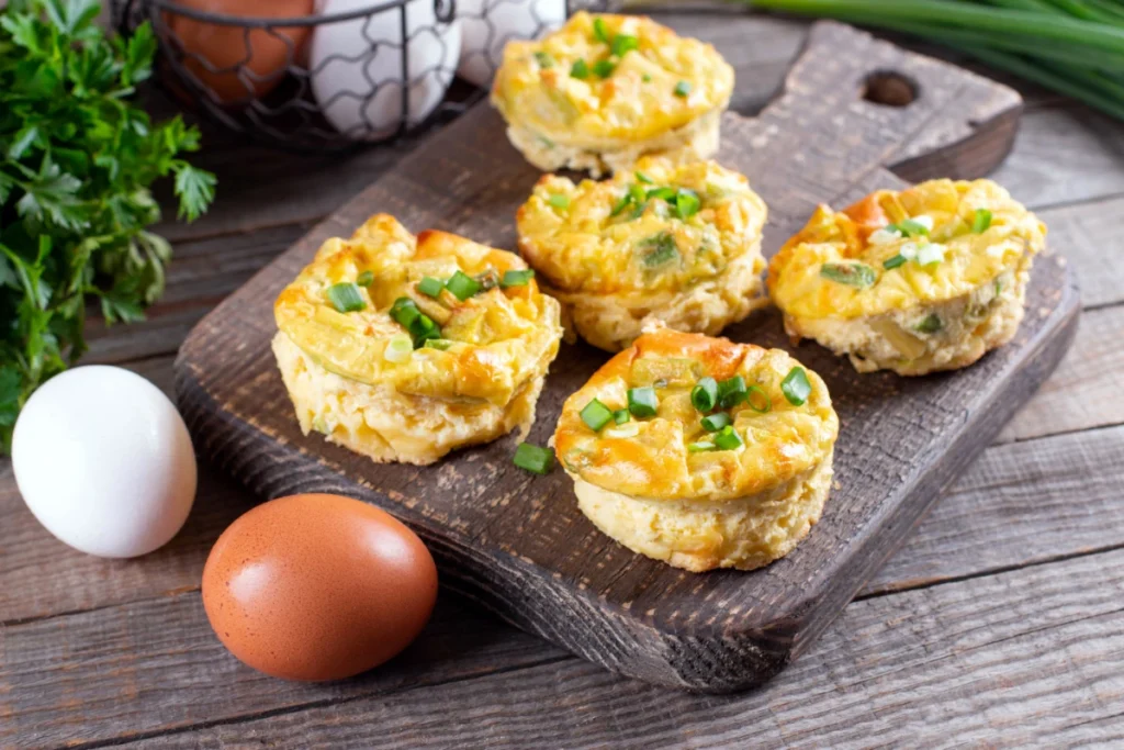 Close-up view of Starbucks-inspired egg bites presented on a wooden cutting board, garnished with green onions. The egg bites feature a smooth, creamy texture visible in the golden tops.