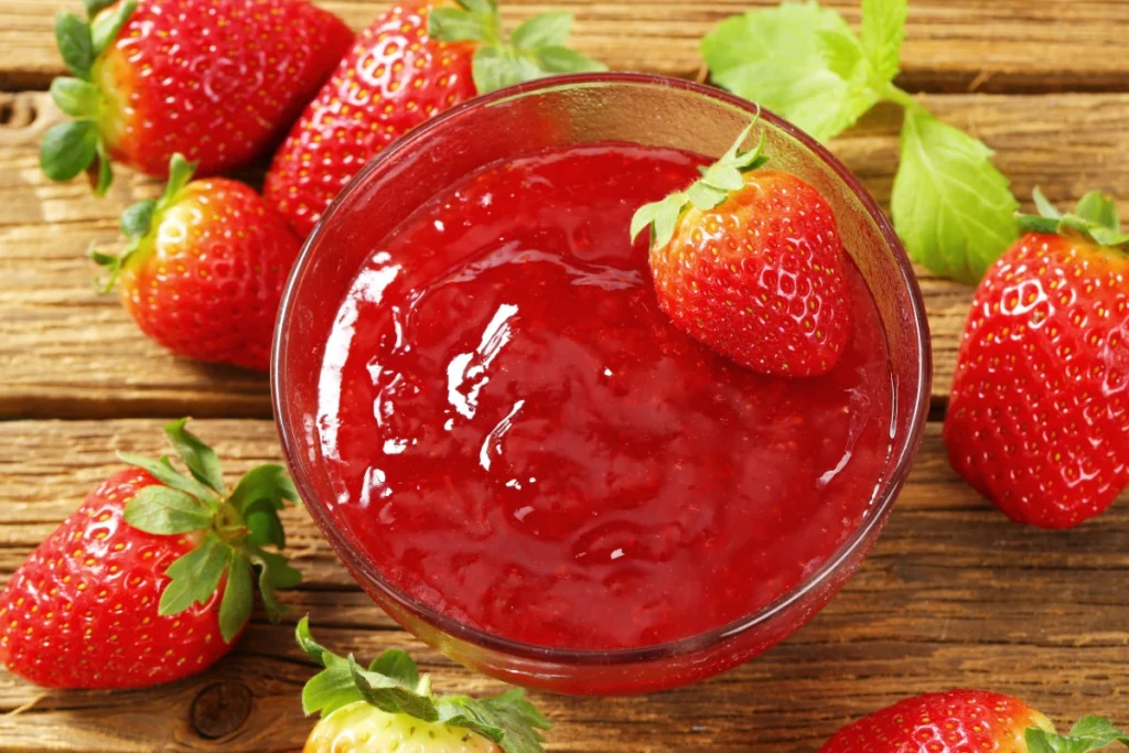 Close-up of a bowl of strawberry puree surrounded by whole strawberries on a wooden surface.