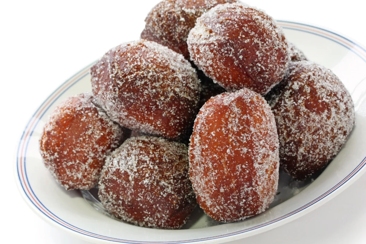 A plate of malasadas, dusted with granulated sugar, against a white background.