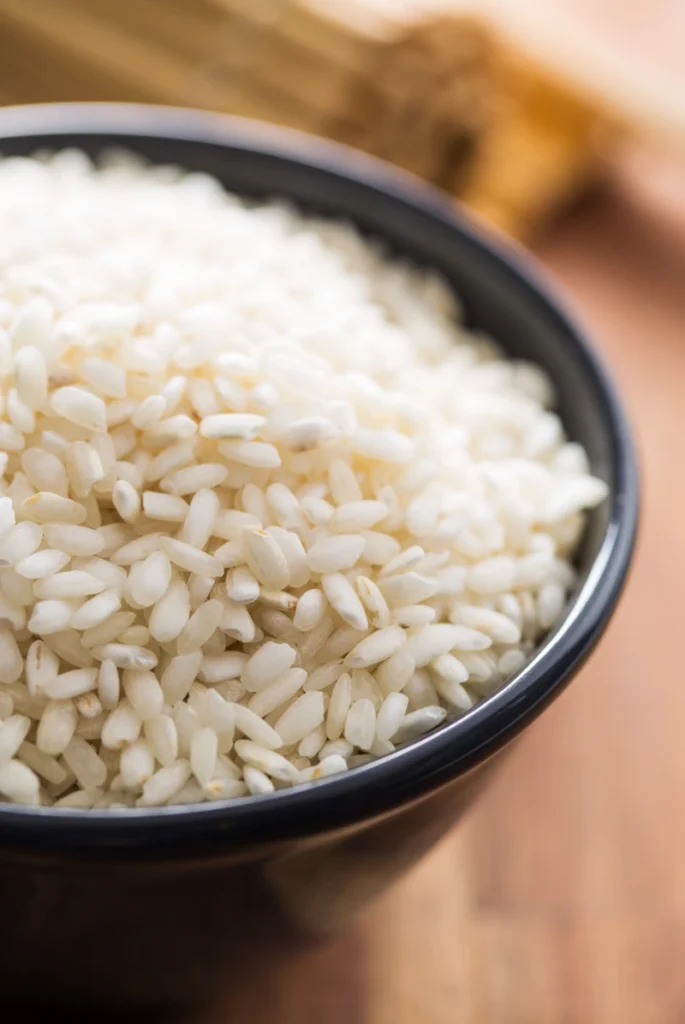 A black bowl filled with uncooked Arborio rice.