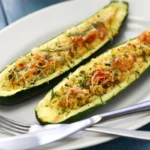 Two zucchini halves stuffed with a mix of rice, vegetables, and cheese, garnished with herbs, presented on a white oval plate with a fork beside it.